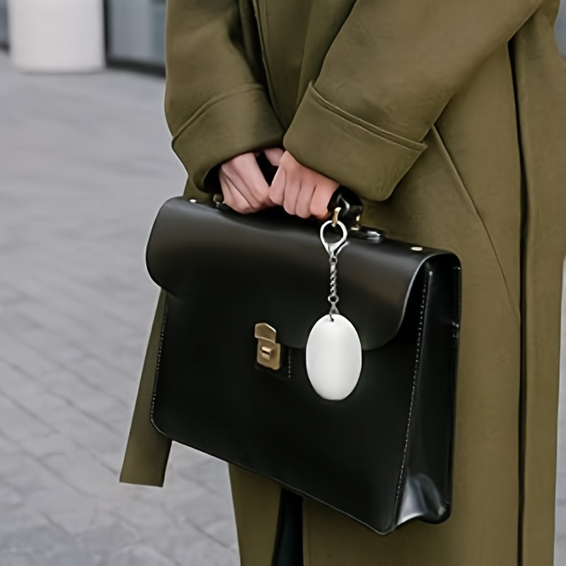 Teardrop-shaped Bluetooth key finder clipped to a black handbag carried outdoors