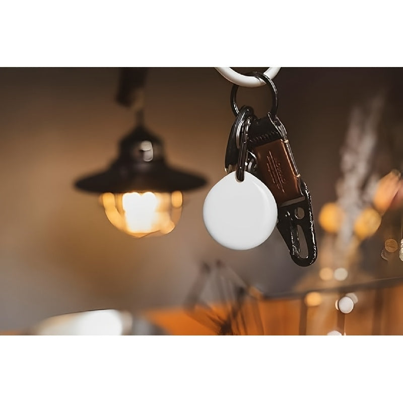 Round white Bluetooth tracker hanging on a keychain against a wall